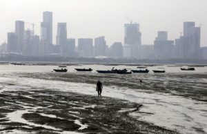 A man walks during low tide at Lau Fau Shan, famous for its oyster culture, in Hong Kong's rural New Territories July 3, 2015. The fast developing city of Shenzhen on mainland China is seen in the background. REUTERS/Bobby Yip - RTX1IXIL